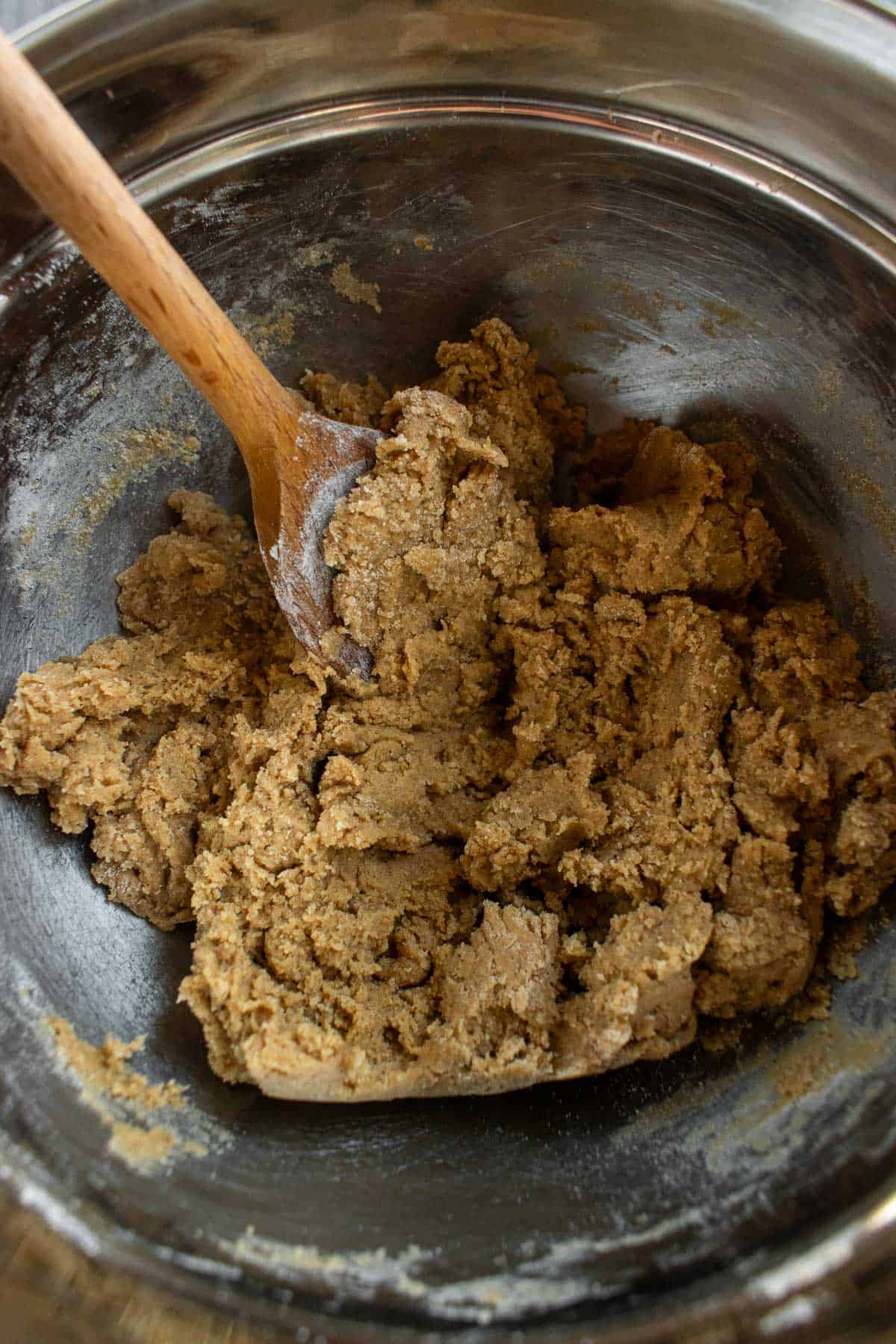 A soft, light brown cookie dough in a mixing bowl with a wooden spoon.