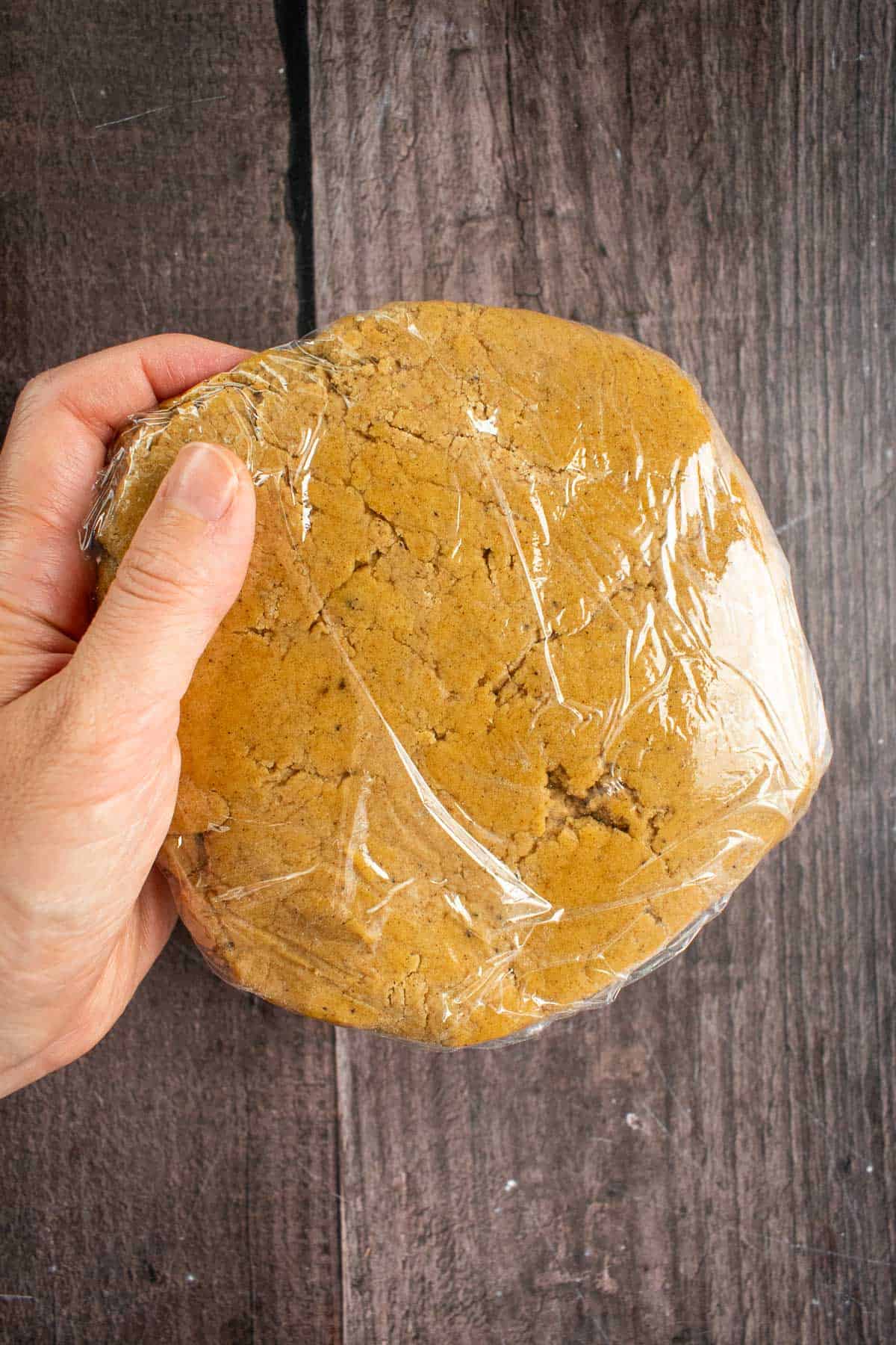 A hand holding brown cookie dough wrapped in plastic wrap.