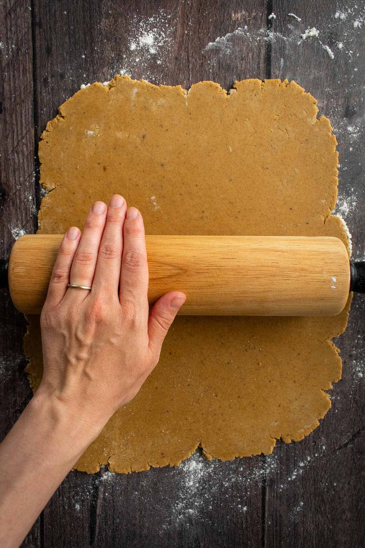 A hand rolling out cookie dough with a wooden rolling pin.
