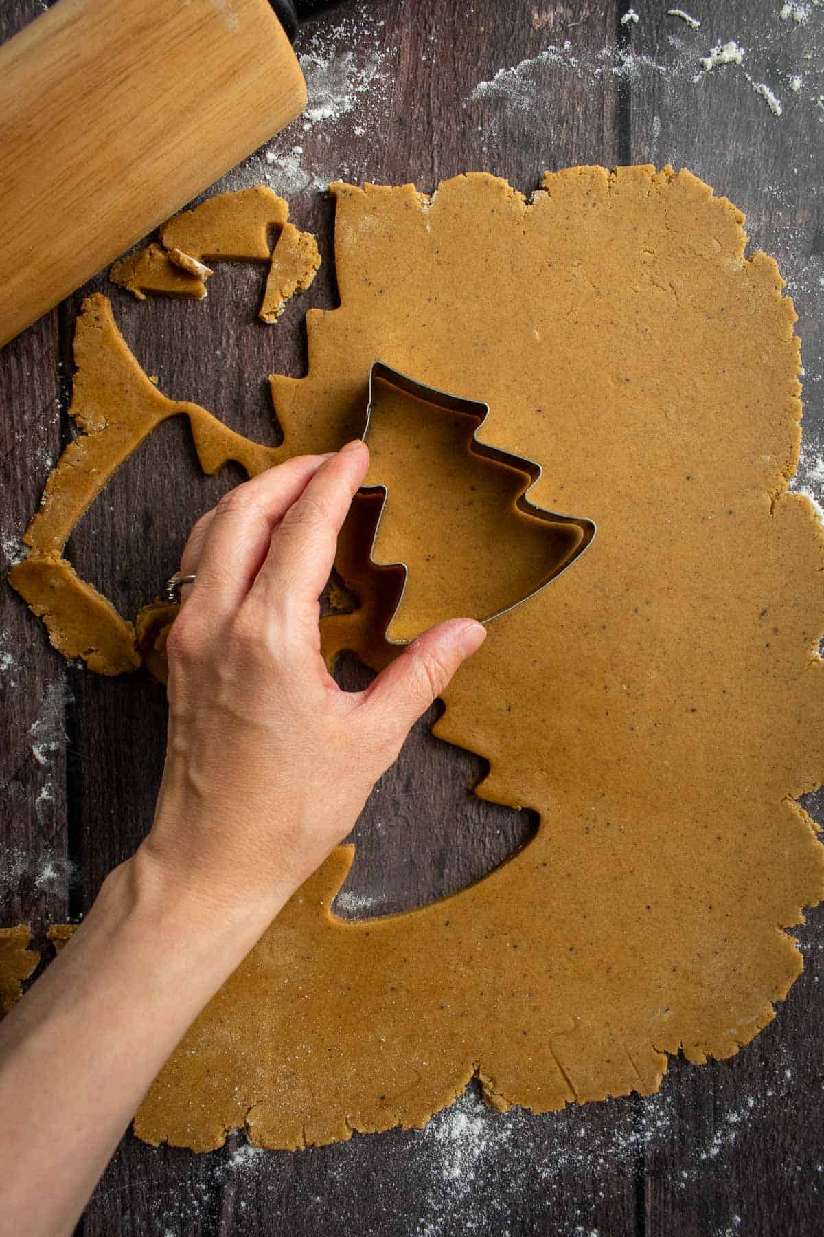 A hand cutting out tree-shaped cookies with metal cookie cutters.