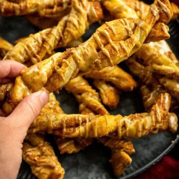 A hand holding a puff pastry cinnamon twist.