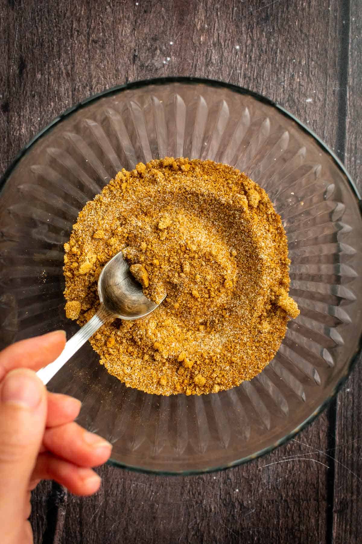 A hand stirring sugar and cinnamon in a bowl with a spoon. 
