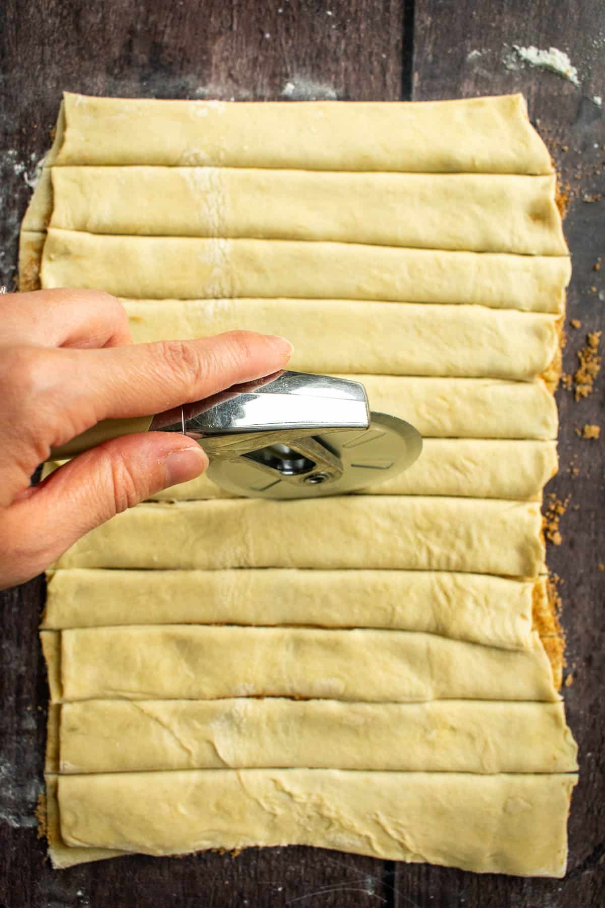 A hand using a pizza cutter to cut strips of puff pastry. 