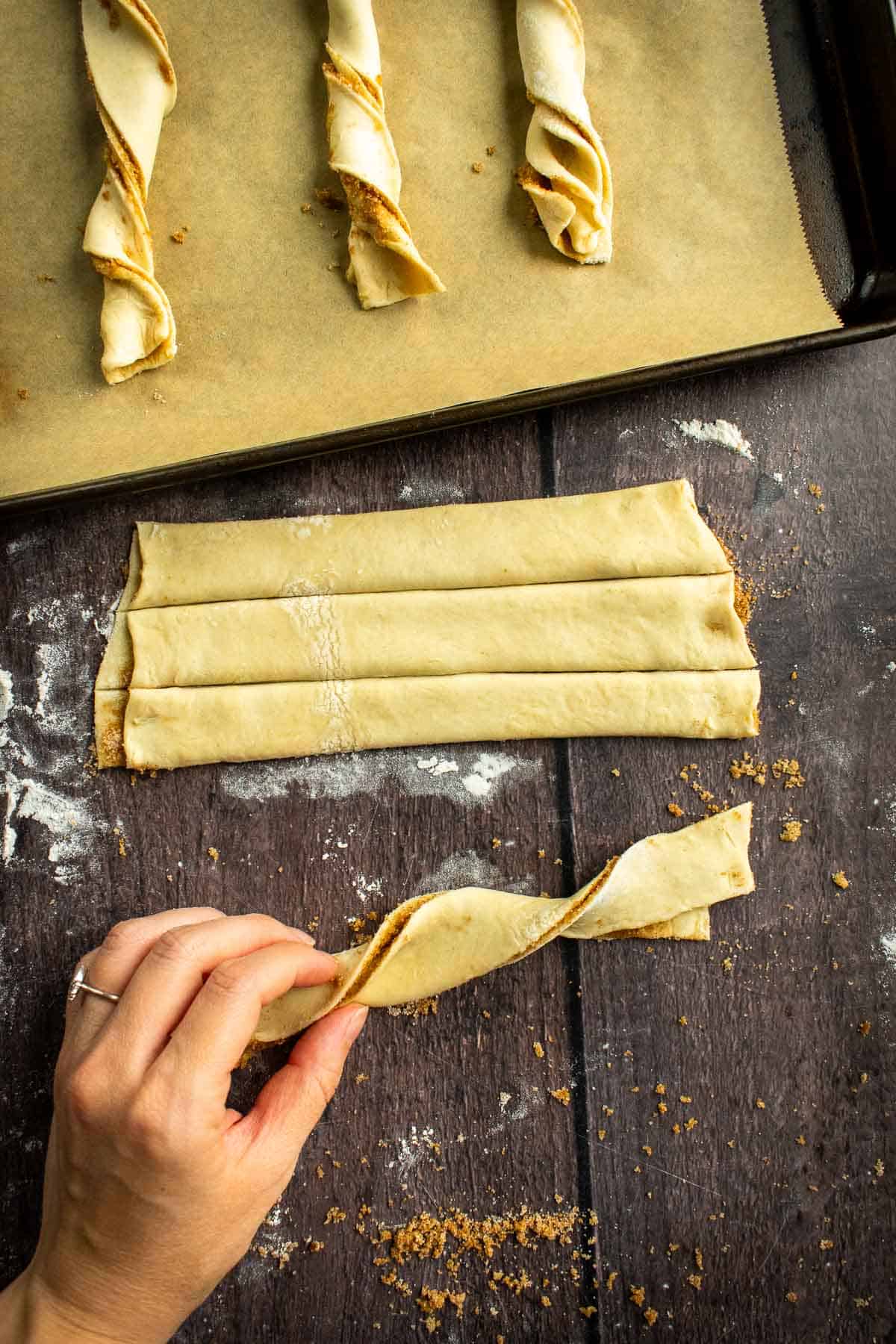 A hand twisting a strip of puff pastry sandwiched with cinnamon sugar.