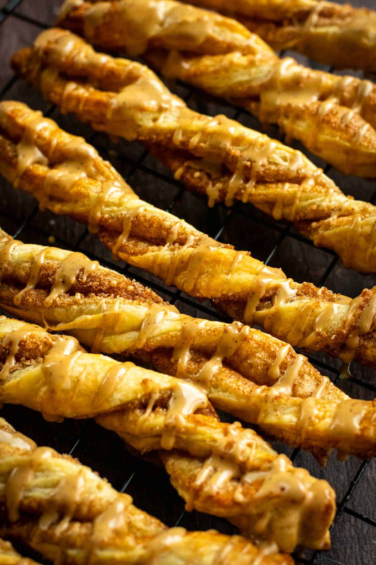 Half a dozen puff pastry twists on a cooling rack topped with brown glaze.