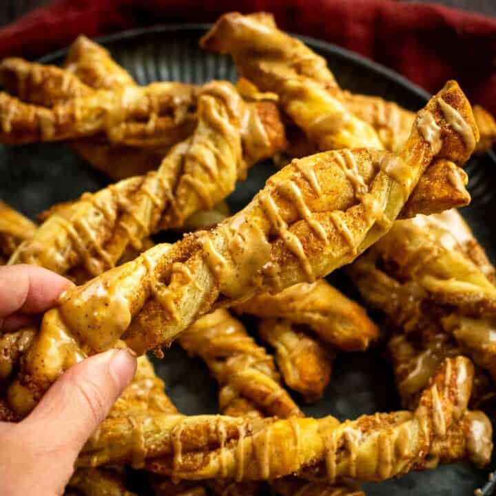 A hand holding a twisted pastry drizzled with espresso glaze.