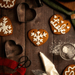 Heart-shaped cookies decorated with white icing next to cookie cutters and icing in a piping bag.