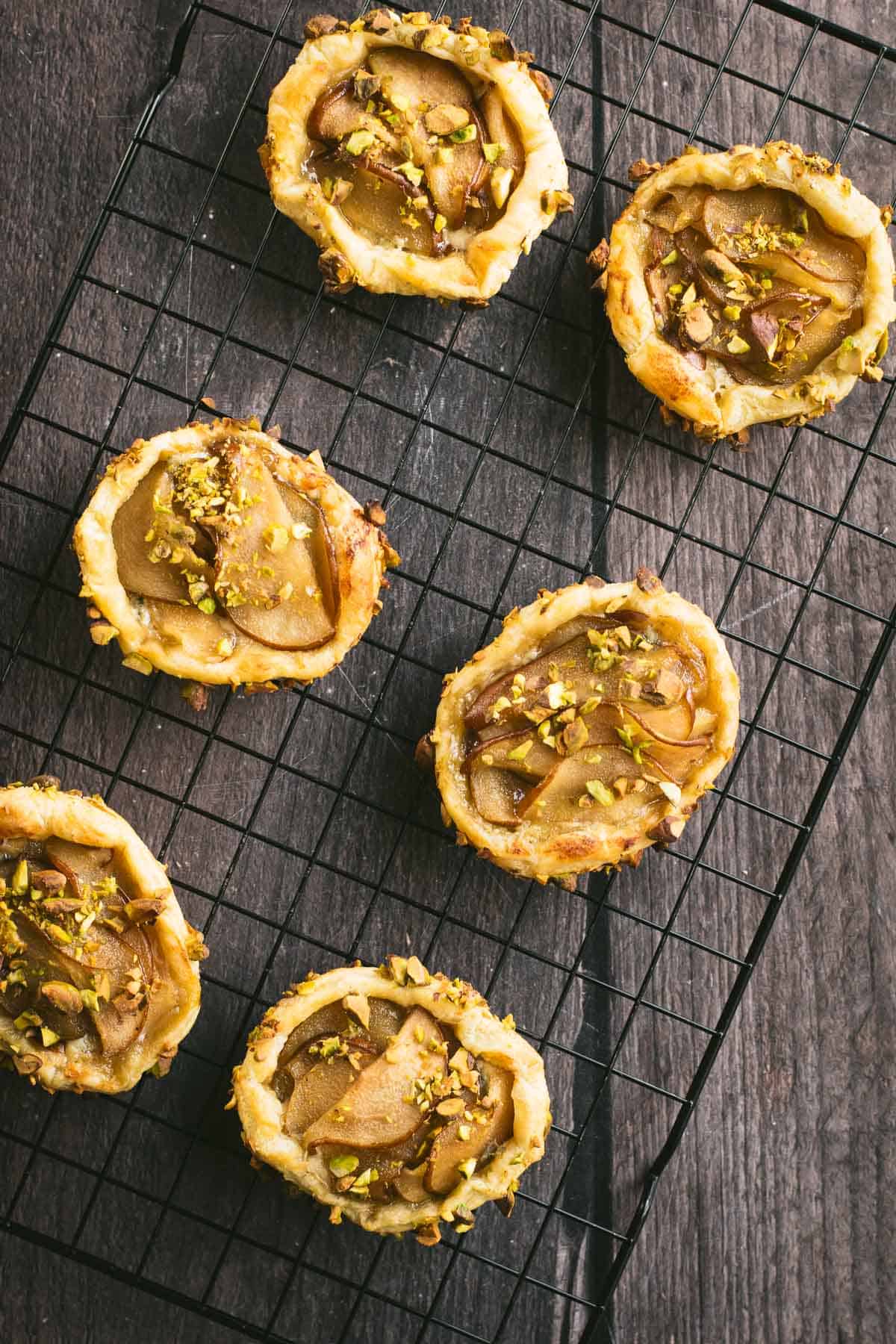 Half a dozen baked pear tarts on a wire cooling rack.