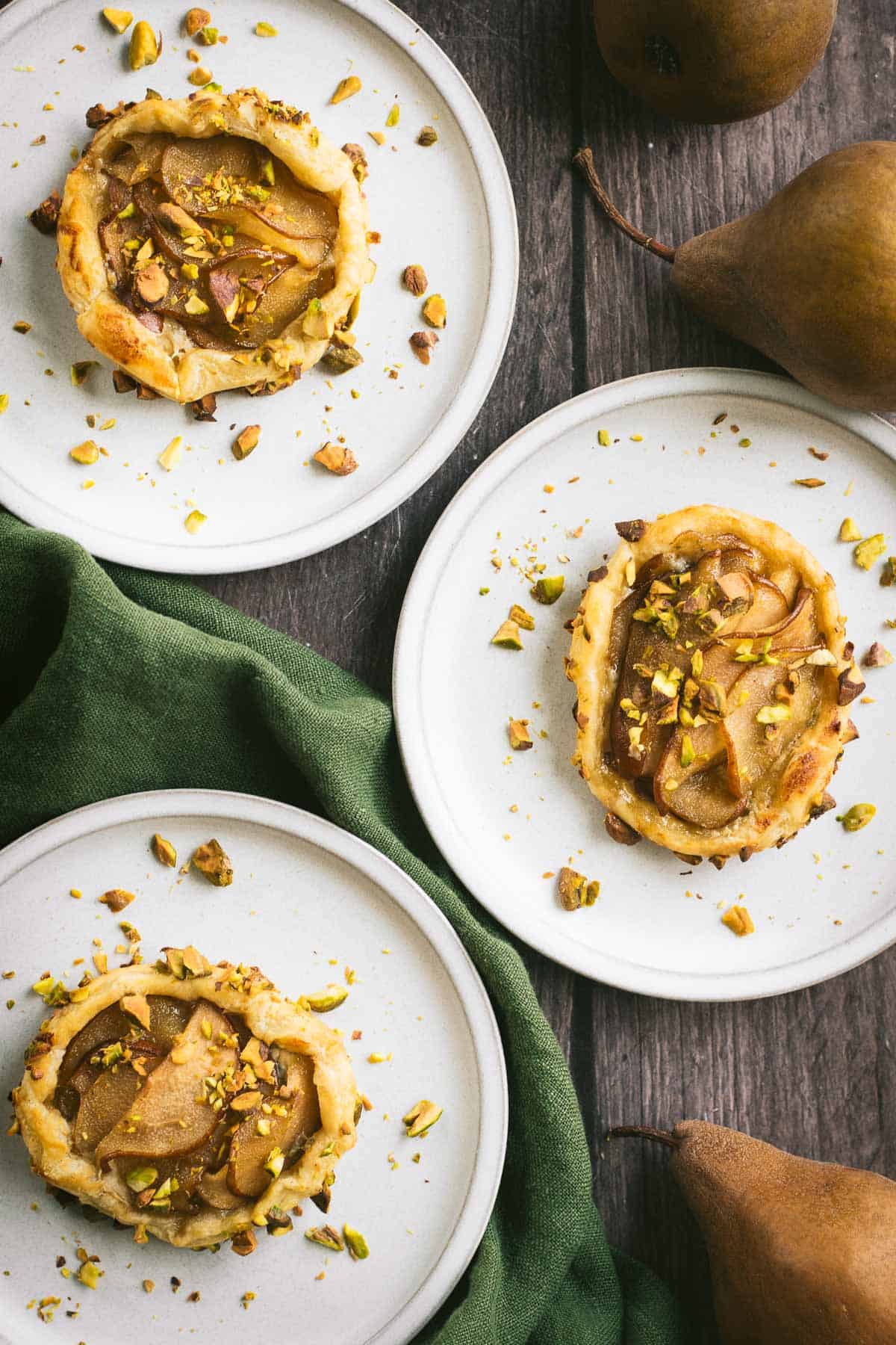 Three pear puff pastry tarts on small grey plates.