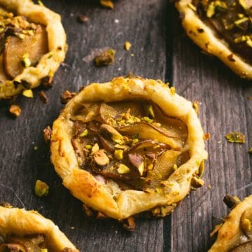 Half a dozen puff pastry pear tarts on a wooden table.