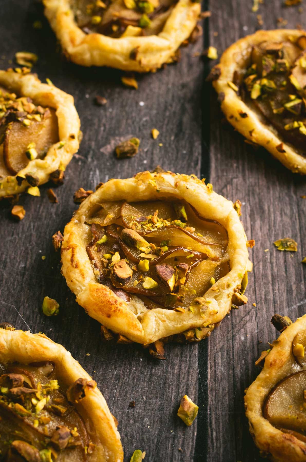 Half a dozen puff pastry pear tarts on a wooden table.