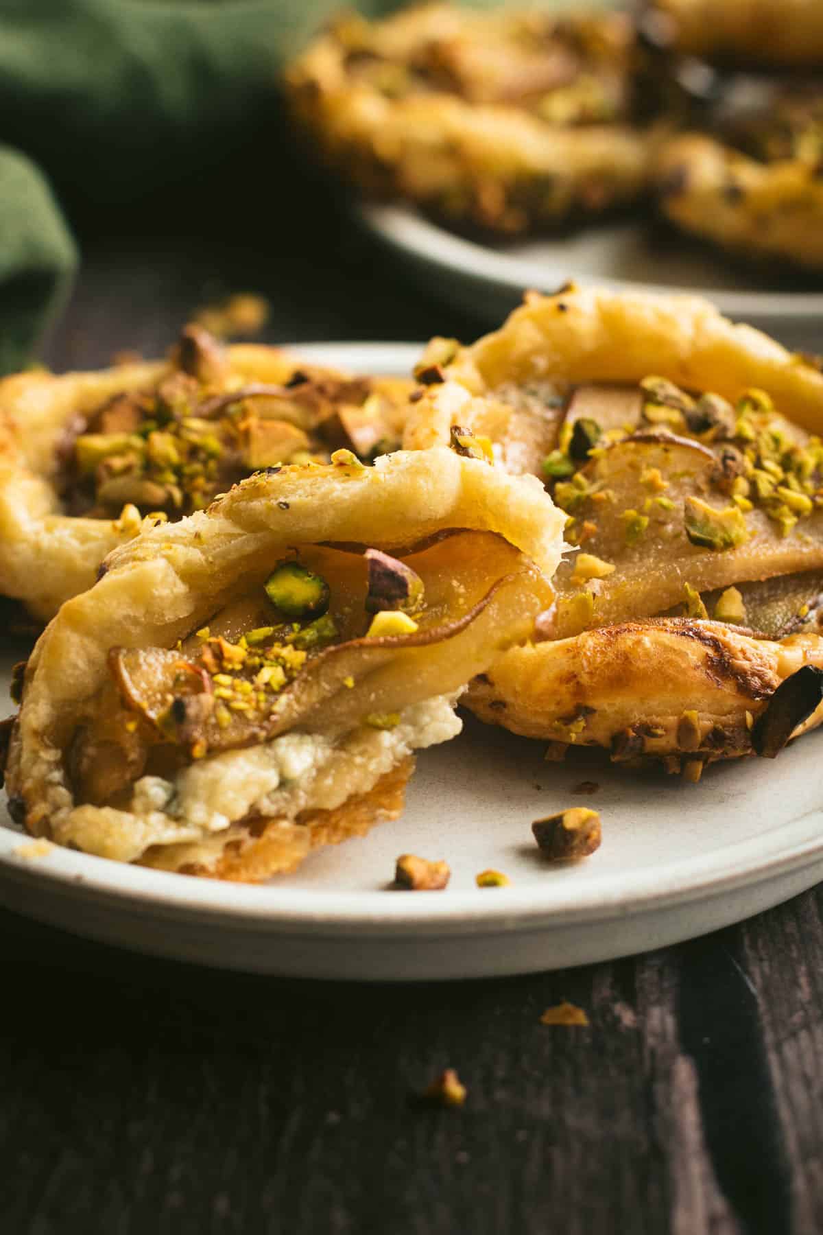 A half-eaten pear and blue cheese tart on a plate with more tarts.
