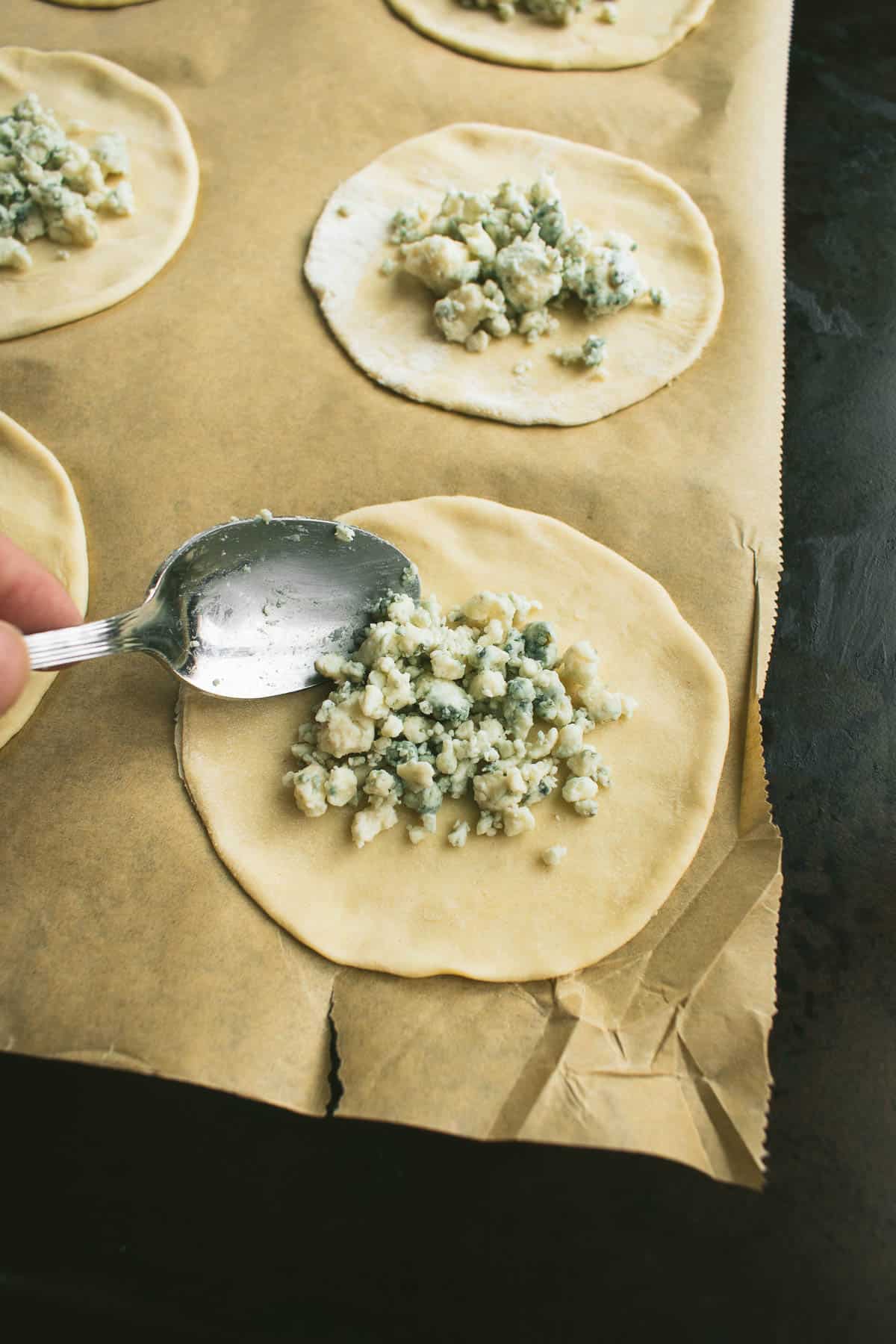 A spoon pouring blue cheese onto a circle of pastry dough.