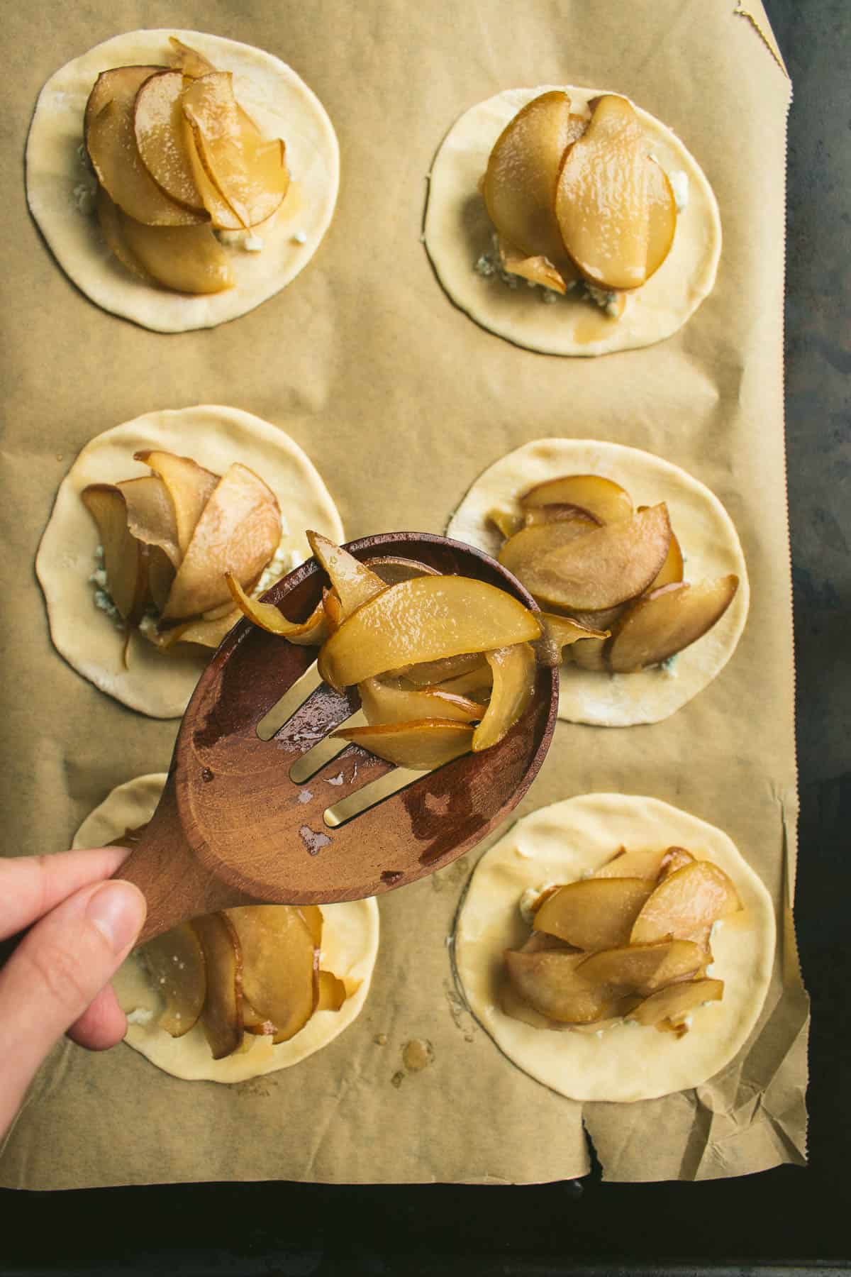 A hand holding a slotted spoon full of caramelized pears.