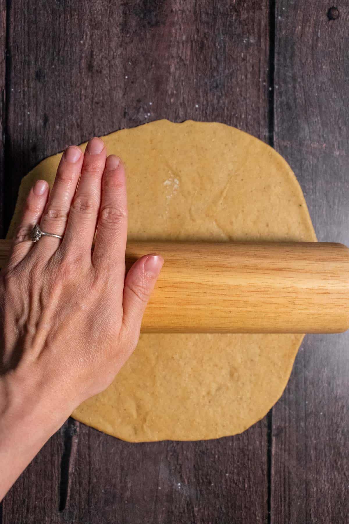 A hand rolling out bread dough with a rolling pin.
