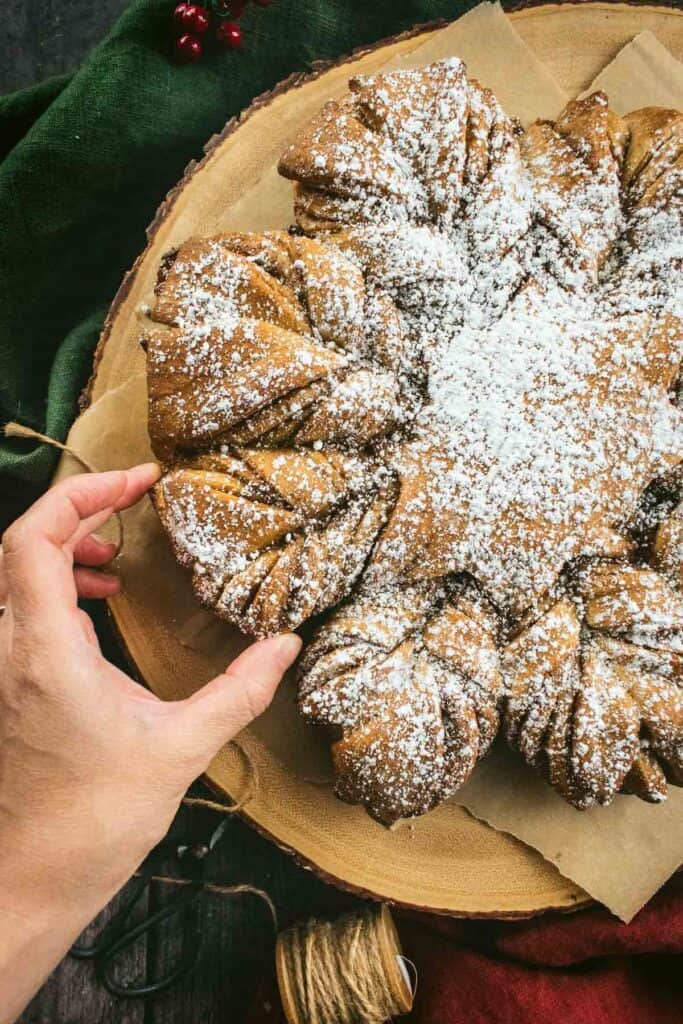 A hand picking up a piece of twisted cinnamon bread.