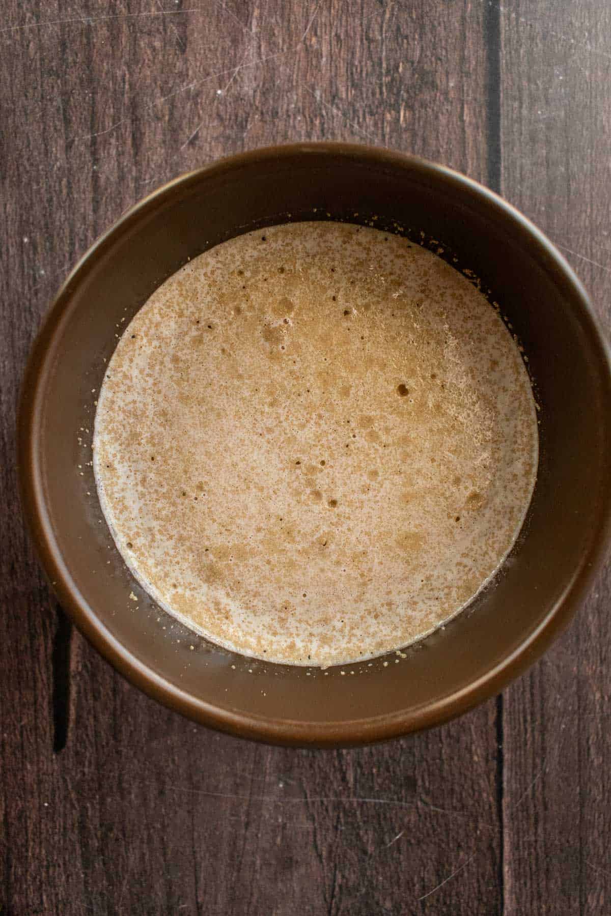 Frothy yeast, milk, and sugar in a brown bowl.