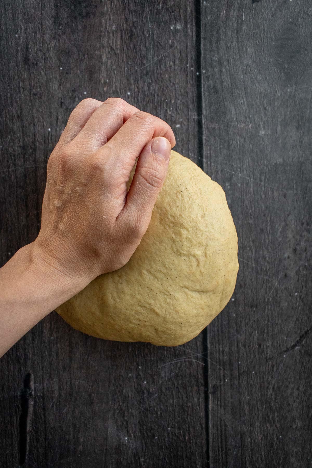 A hand kneading a ball of bread dough on a table.