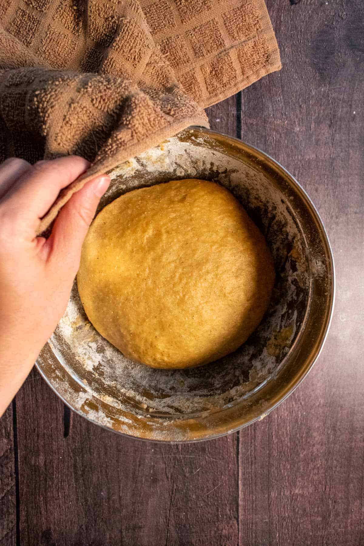 Risen bread dough in a mixing bowl partially covered by a towel. 