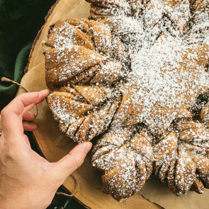 A hand tearing off a piece of twisted cinnamon bread from the loaf.