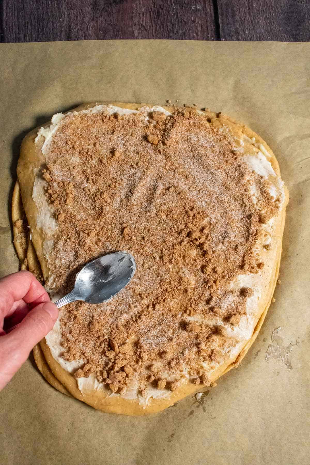 A hand spreading cinnamon sugar on rolled-out bread dough. 