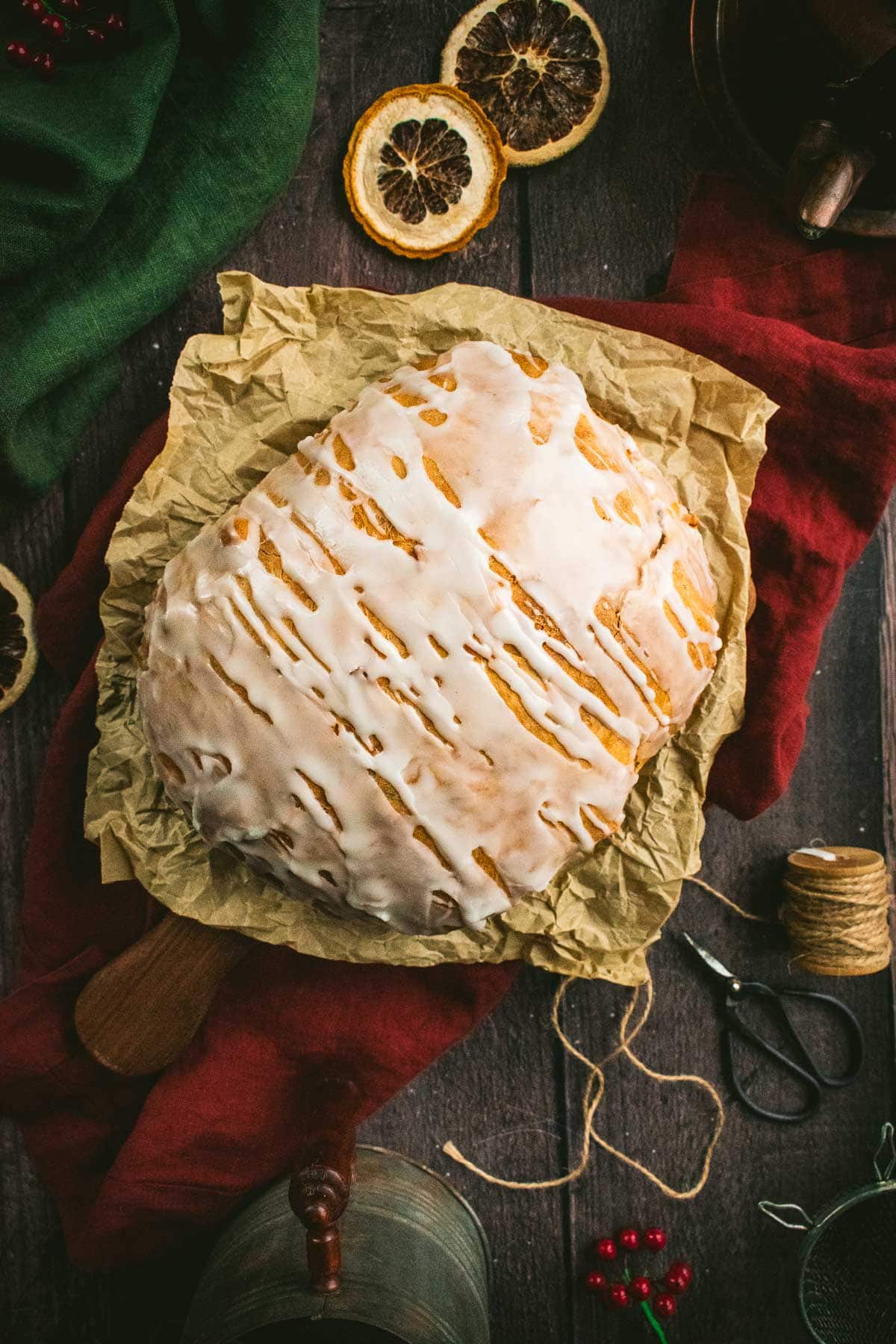 A baked loaf of bread topped with white glaze on parchment paper.