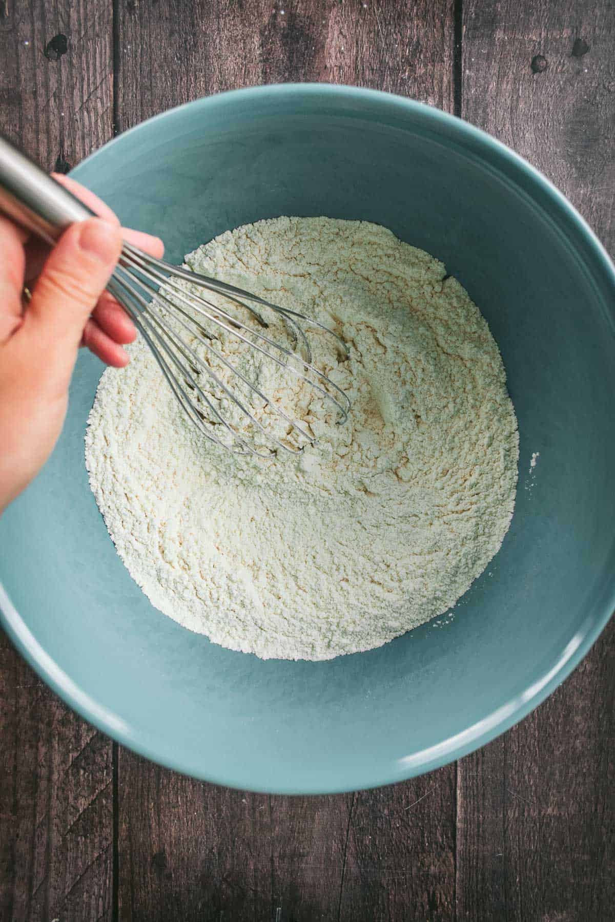 A hand whisking flour and salt in a mixing bowl.