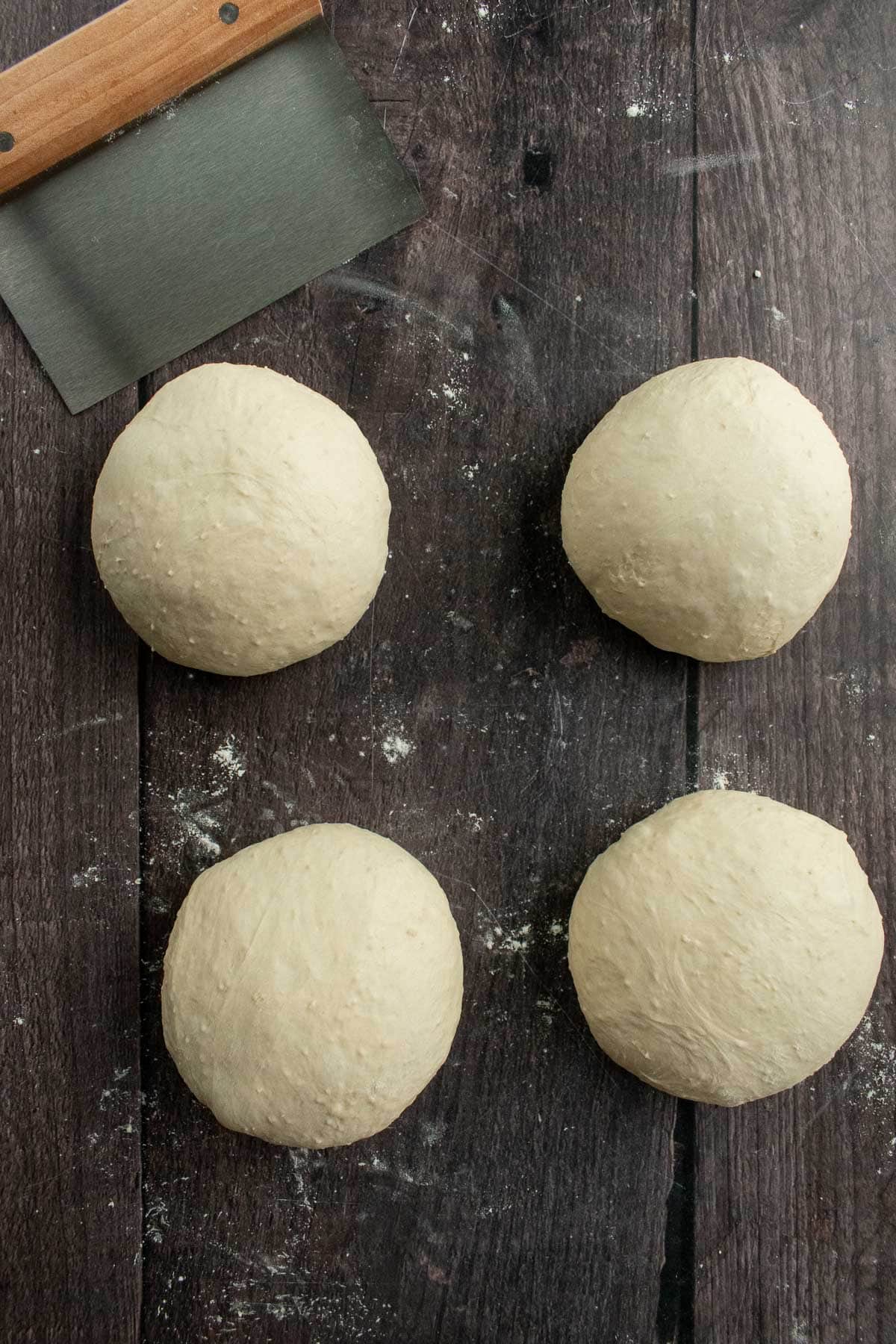 Four small balls of dough on a wooden table.