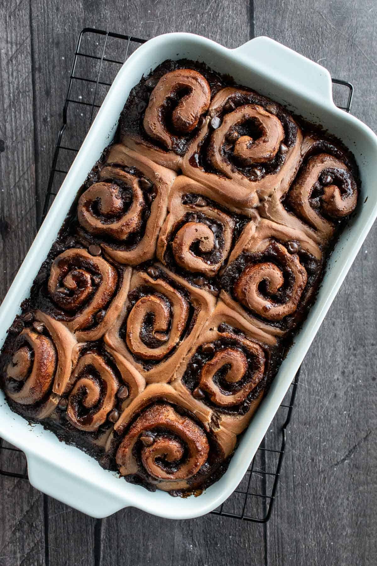 A dozen baked dark brown cinnamon buns in a blue baking dish.