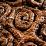 Baked chocolate cinnamon rolls with brown glaze drizzled on top.