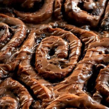 Half a dozen baked chocolate cinnamon rolls in a pan topped with brown glaze.