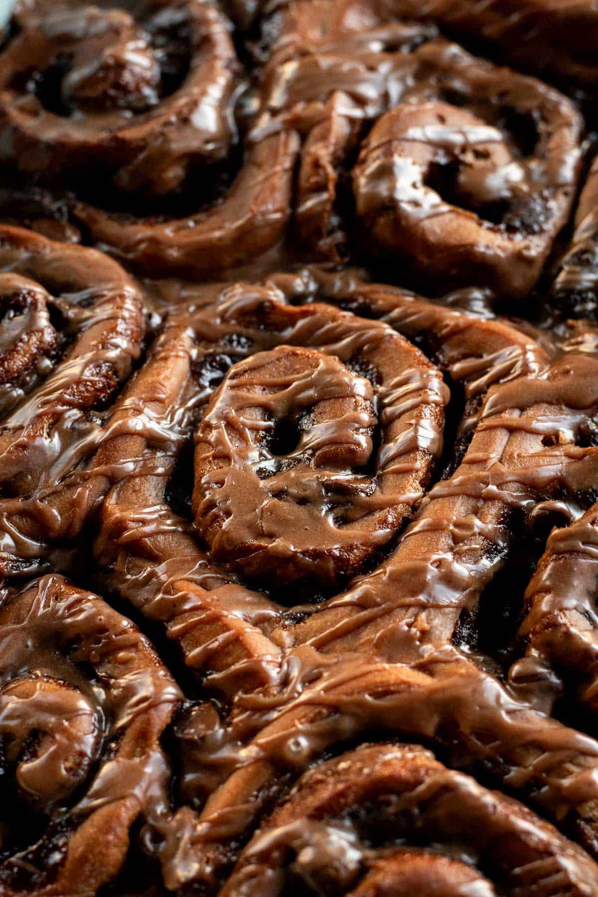 Half a dozen baked chocolate cinnamon rolls in a pan topped with brown glaze.