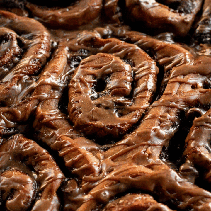 Baked chocolate cinnamon rolls with brown glaze drizzled on top.