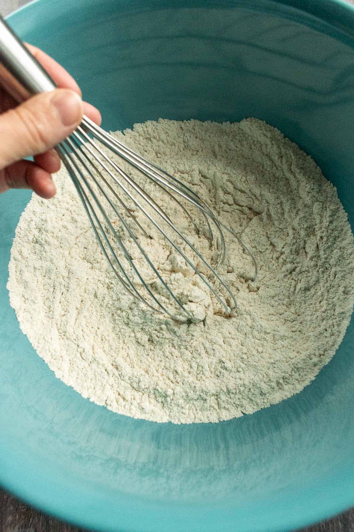 A hand whisking flour in a blue bowl.