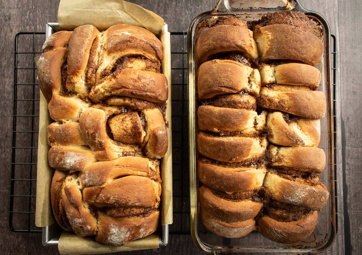 Two loaves of cinnamon roll bread in loaf pans on a cooling rack.