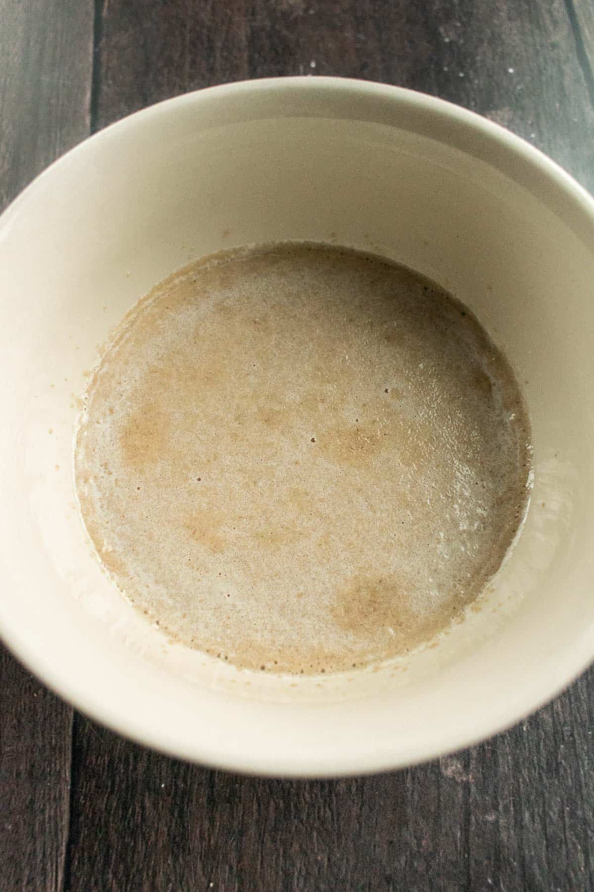 Frothy milk, sugar, and yeast in a beige bowl.