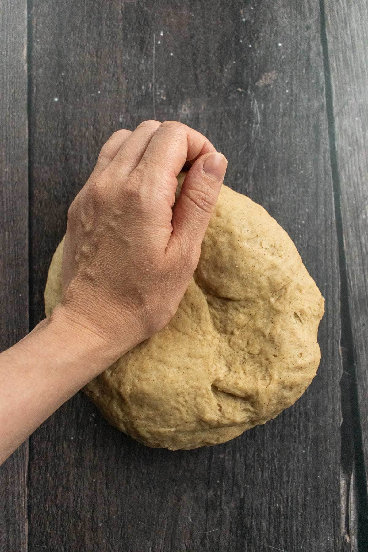 A hand kneading a ball of dough on a wooden table.