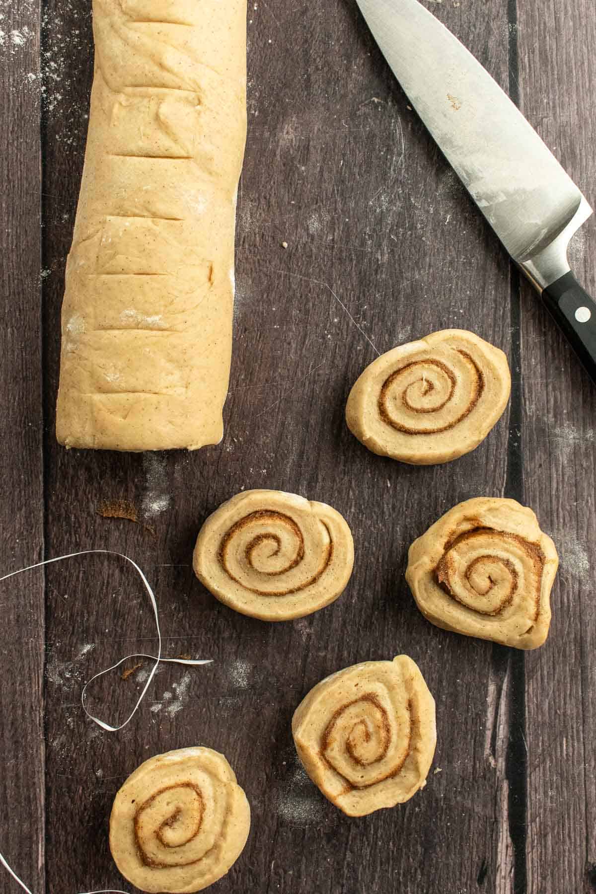 Unbaked cinnamon rolls next to a knife on a wooden table.