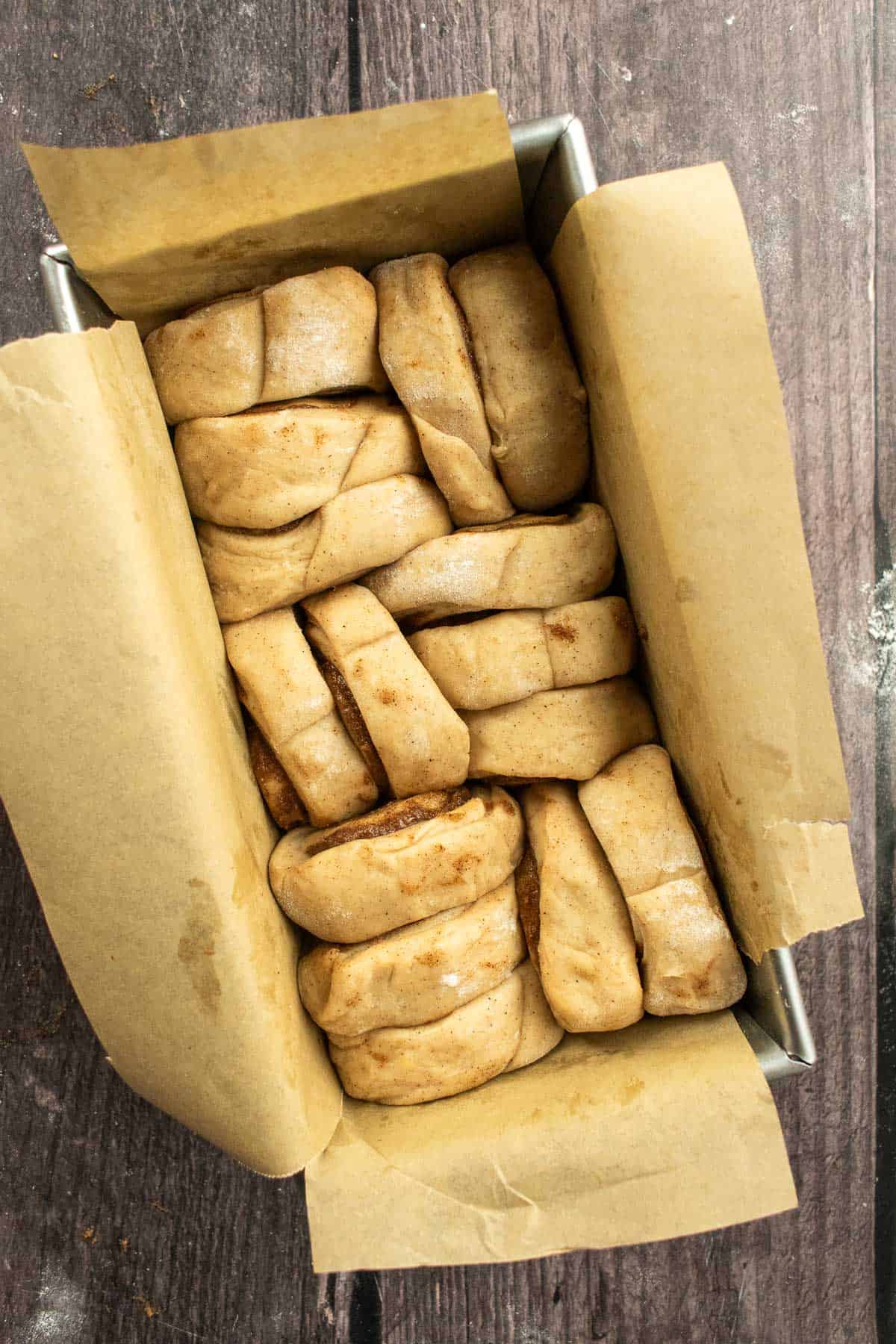 Small cinnamon rolls arranged in a loaf pan lined with parchment paper.