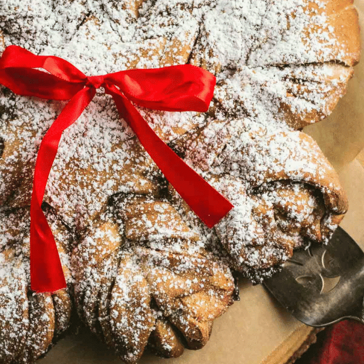 A twisted cinnamon star bread on a wooden board topped with powdered sugar.