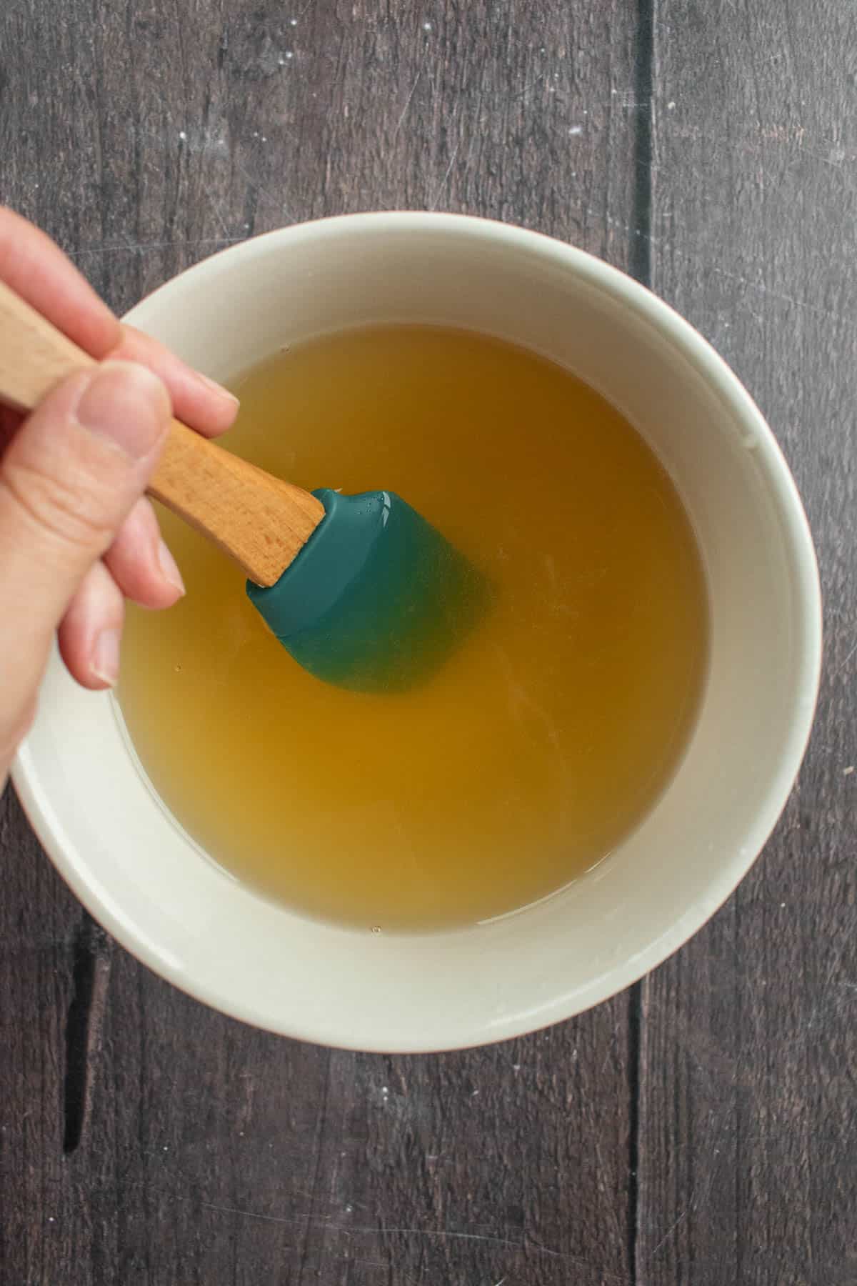 A hand mixing honey and water in a small bowl.