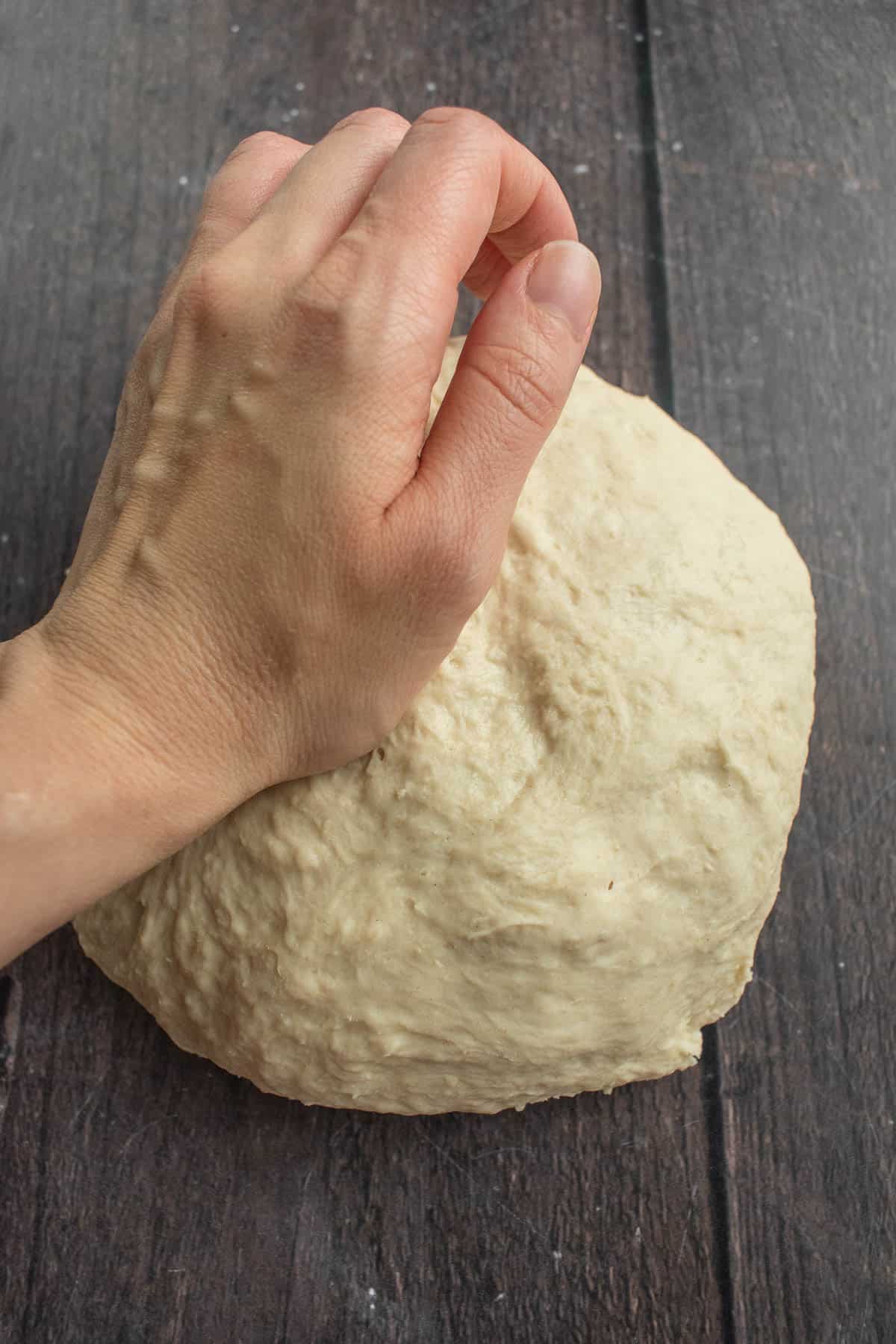 A hand kneading bread dough on a table.