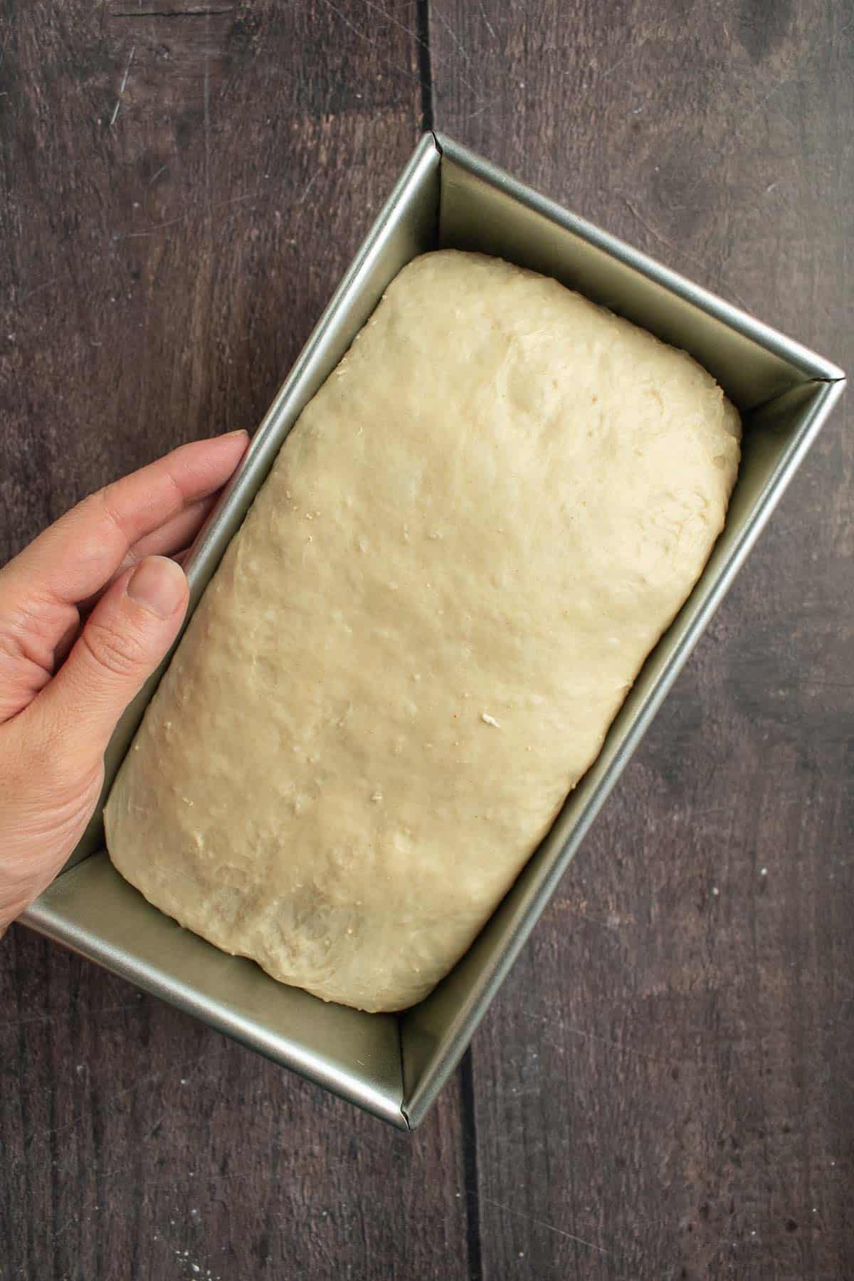 An unbaked loaf of white bread in a metal loaf pan.