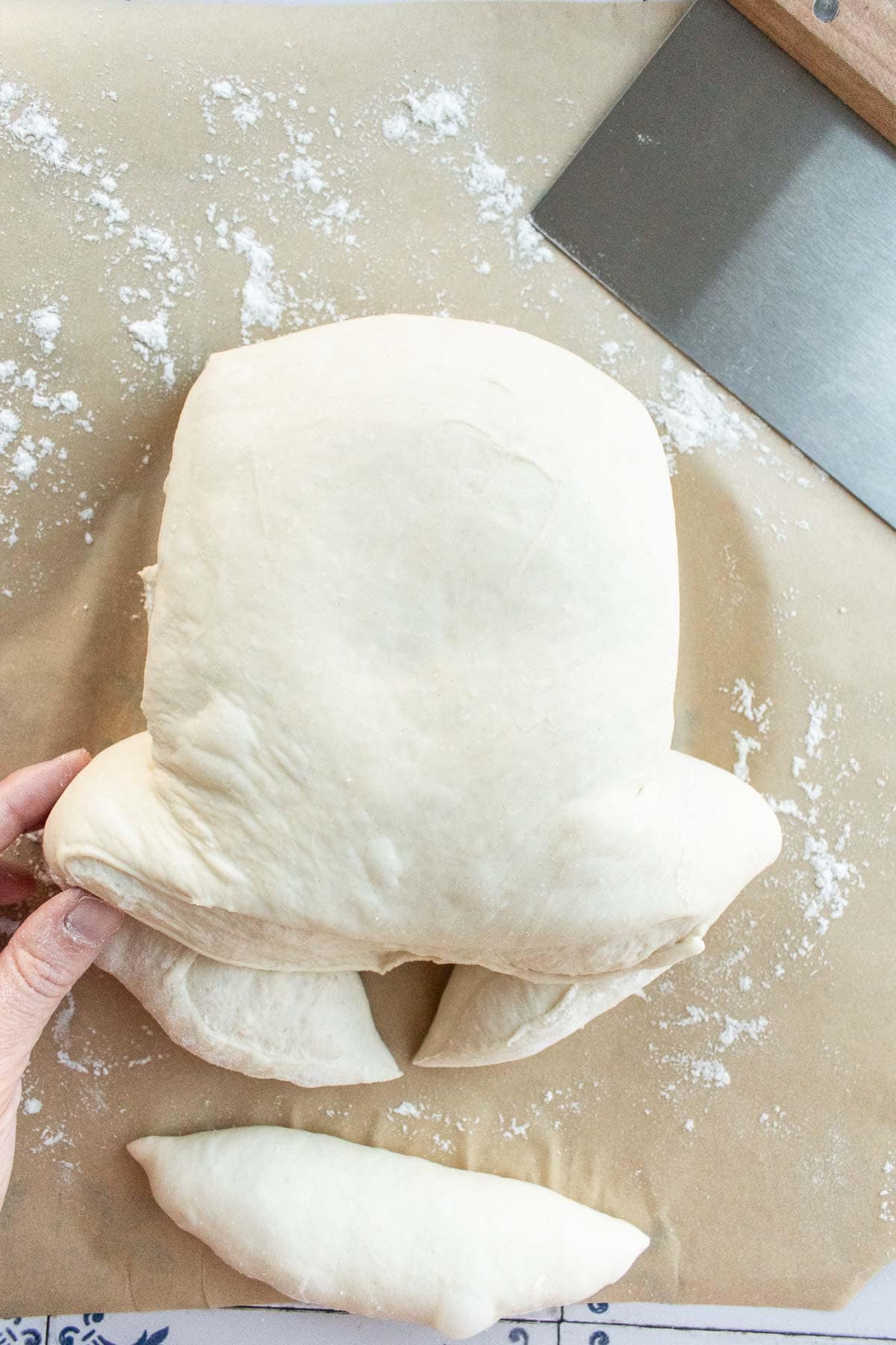 A hand tucking two pieces of bread dough underneath itself.