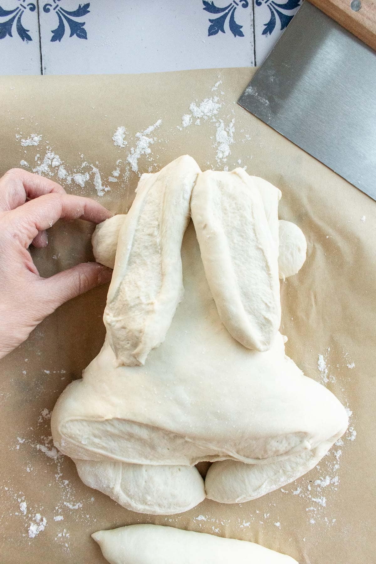 A hand placing two balls of dough underneath a large bunny-shaped bread dough.