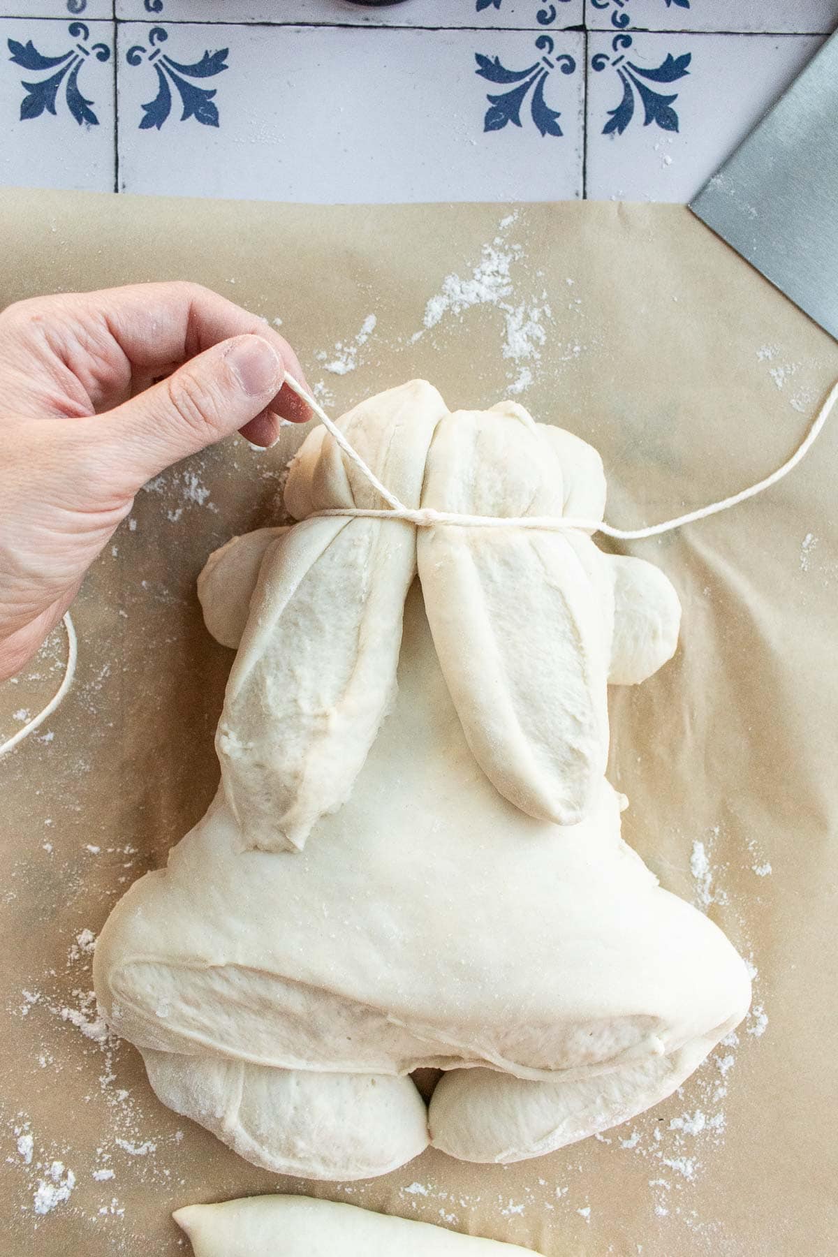 A hand tying baking twine around a loaf of bread dough on parchment paper.