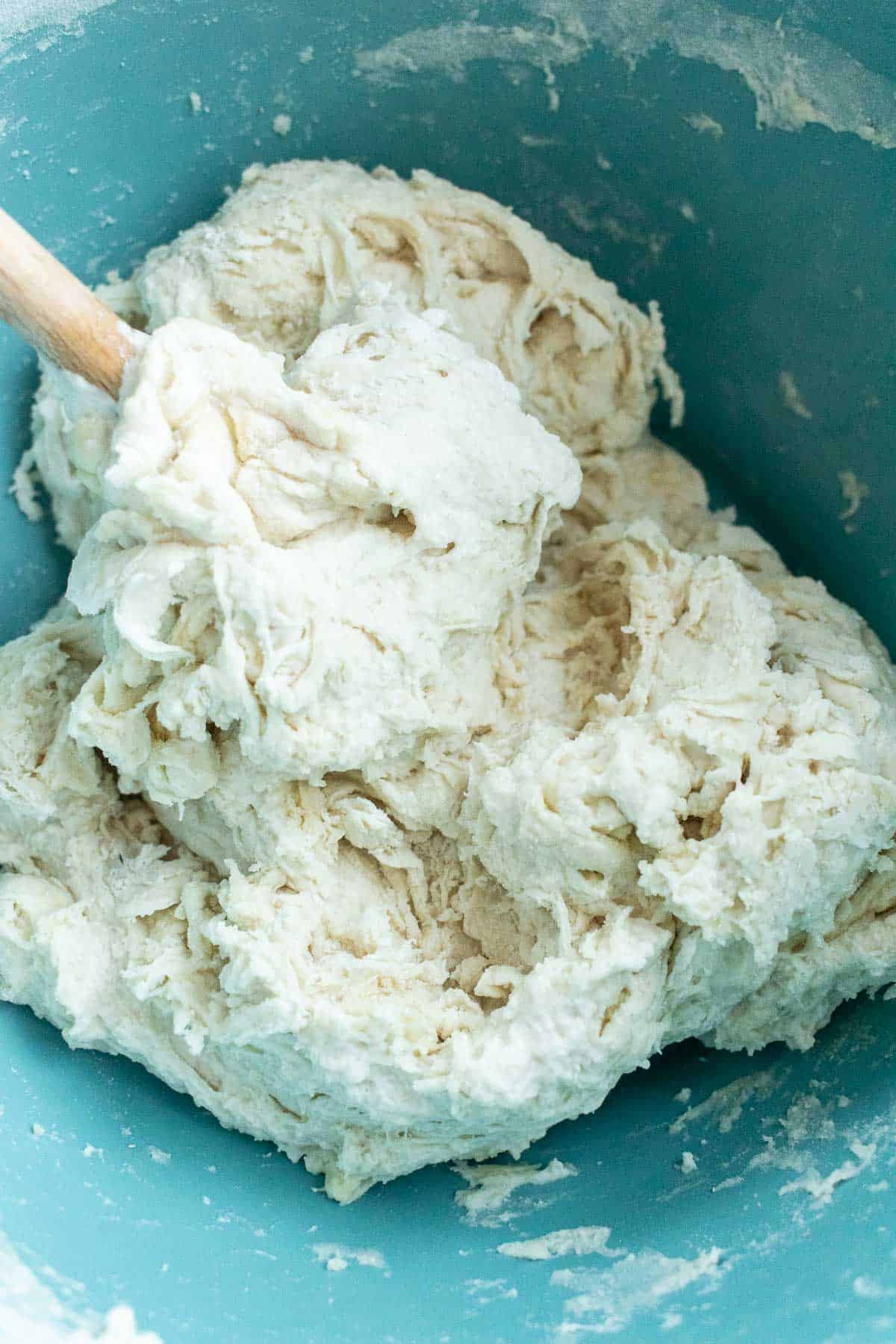 A wooden spoon in a bowl of shaggy bread dough.