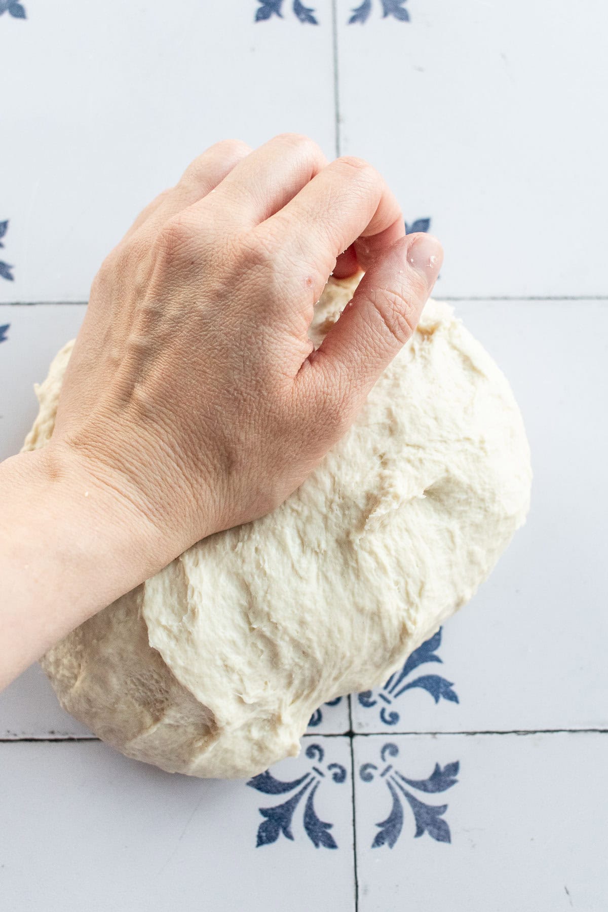 A hand kneading light bread dough on a table.