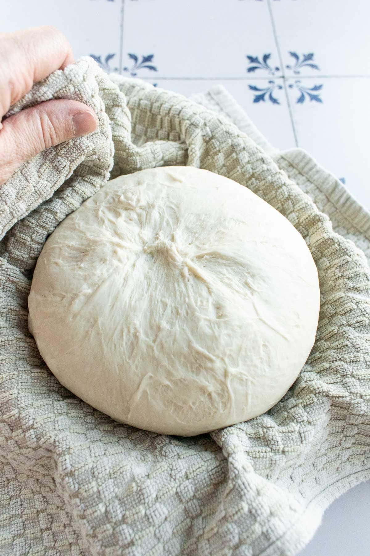 A large boule of bread dough proofing on a towel-lined bowl.