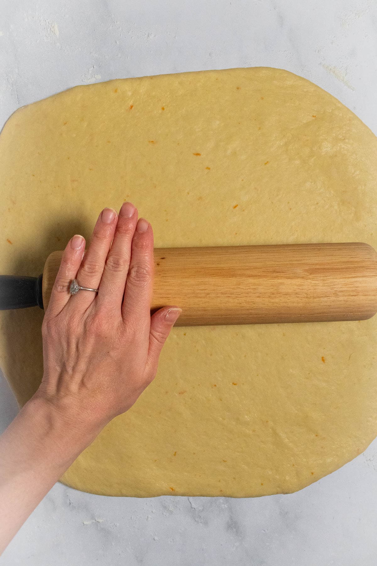 A hand rolling out bread dough with a rolling pin.